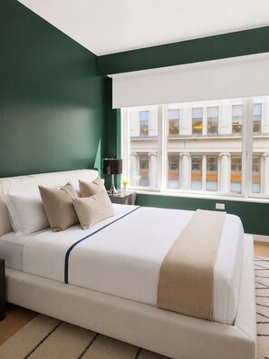 A hotel room with a large bed, a nightstand, a lamp, and a view of a building through a window. - FiDi High-Rise · Skyline Views · Luxury Amenities (New York)