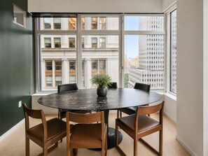 A round table with four chairs, a potted plant, and a view of a cityscape through large windows. - FiDi High-Rise · Skyline Views · Luxury Amenities (New York)