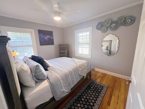 Un dormitorio con cama, ventilador de techo, ventana, espejo y decoración en la pared.