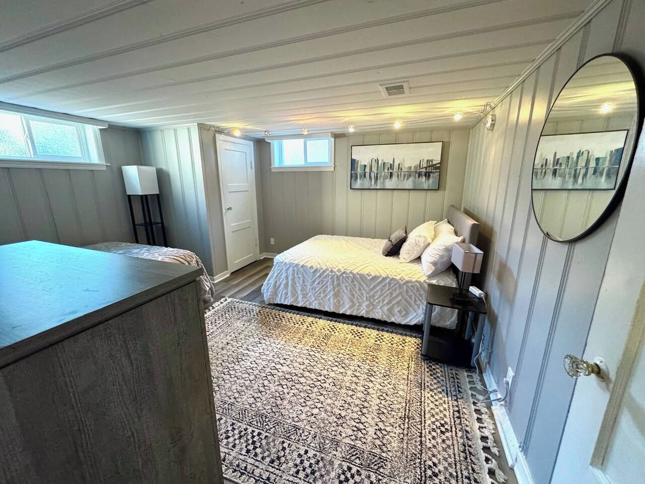 Ein Schlafzimmer mit Bett, Nachttisch, Lampe, Teppich und einem Stadtbild an der Wand.