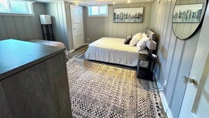 Un dormitorio con cama, mesita de noche, lámpara, alfombra y un cuadro de paisaje urbano en la pared.