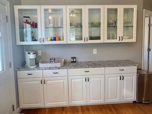 Una cocina con armarios blancos, encimera de granito y un cubo de basura de acero inoxidable.