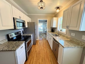A kitchen with white cabinets, a granite countertop, stainless steel appliances, and a wooden floor. - Spacious Retreat: Walk to Midtown Near Dining+Fun (Reno)