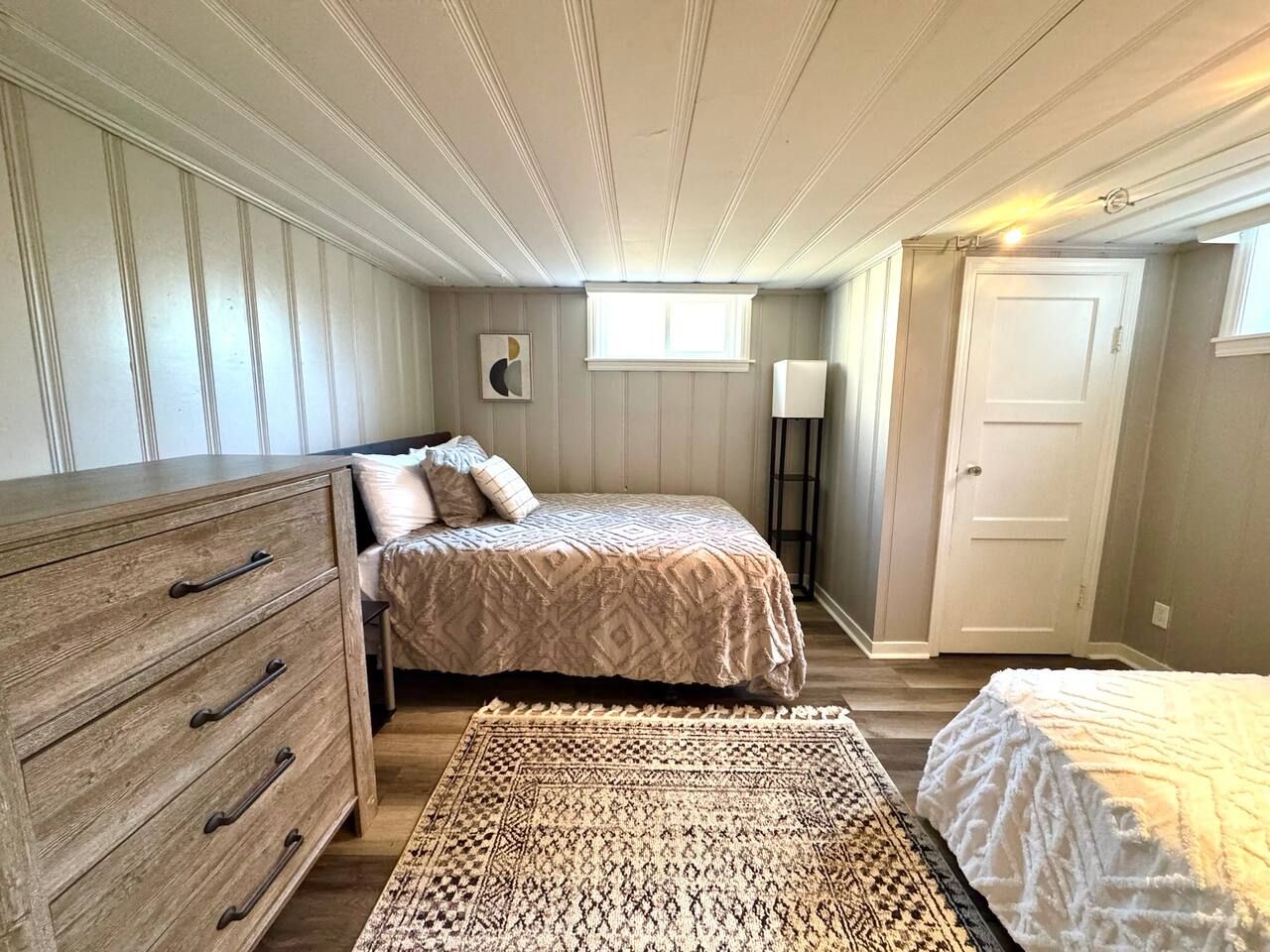 A bedroom with a wooden dresser, a bed with patterned bedding, a rug, and a door.