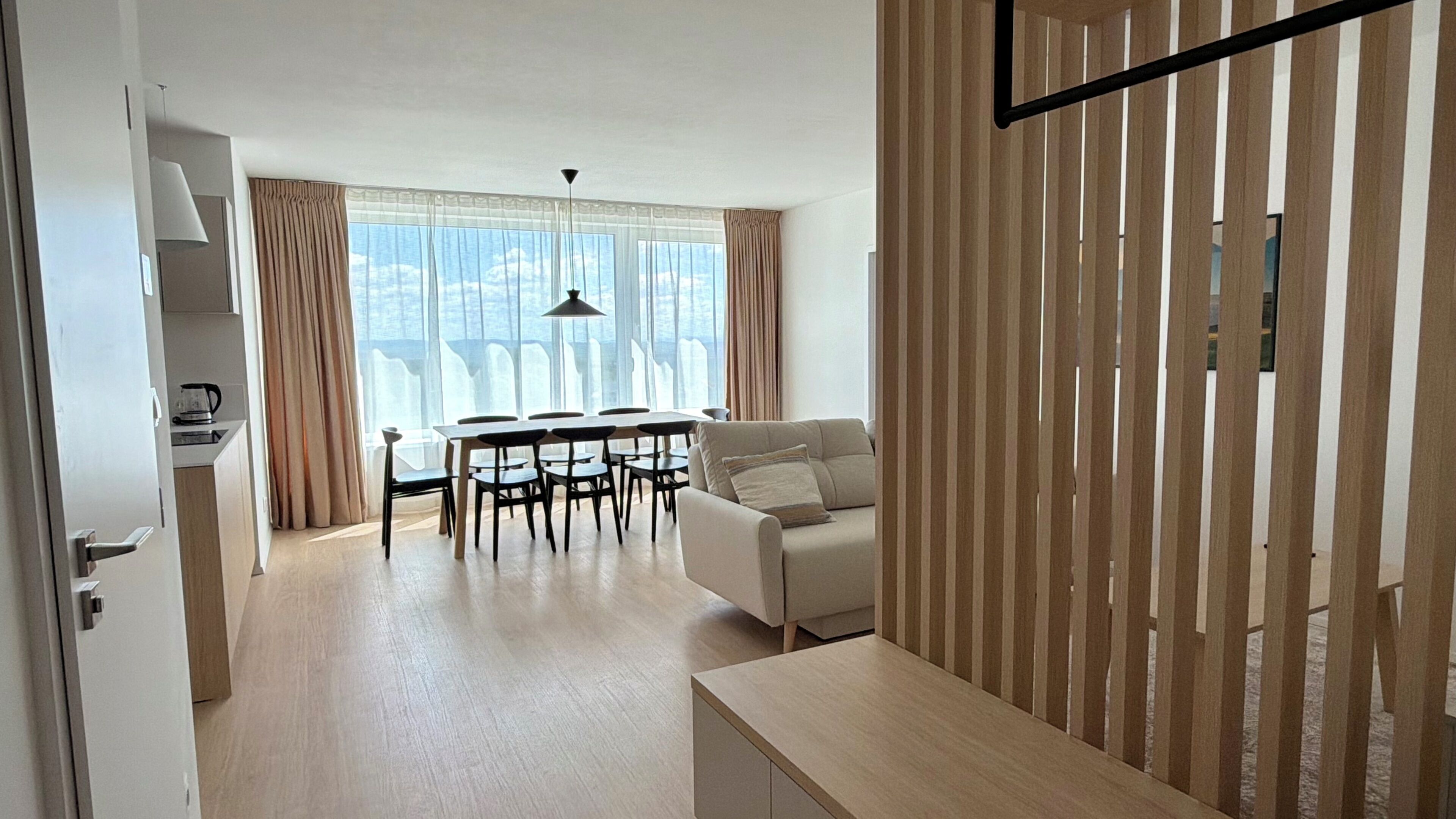 A modern living room with a sofa, a dining table with chairs, and a kitchen area with a kettle.
