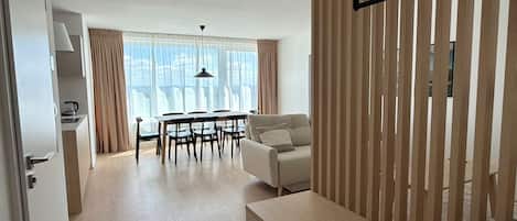 A modern living room with a sofa, a dining table with chairs, and a kitchen area with a kettle.