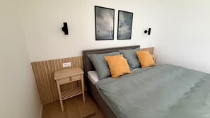 A bedroom with a bed, nightstand, wall-mounted light, and two framed pictures. - Phenomenal 2-bedroom apartment in charming Gerlachov awaits you (Gerlachov)