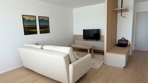 Ein modernes Wohnzimmer mit einer Couch, einem Couchtisch, einem Flachbildfernseher und einem kleinen Holznachttisch.