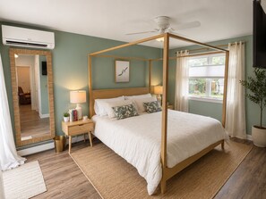 Un dormitorio con cama con dosel, una mesita de noche con lámpara, un espejo y vistas al exterior.