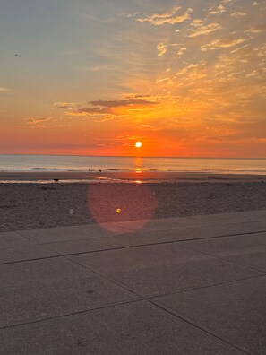 A sunset over a beach with a clear sky and calm sea.