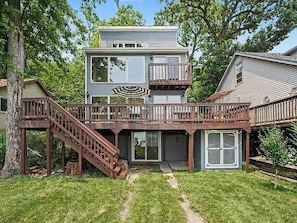 A two-story house with a wooden deck, a staircase, and a garage door. - Cedar Lake Social - 3BR/3BA Waterfront Retreat + Private Dock & Prime Lake Views (Cedar Lake)