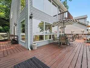 A deck with a table and chairs, a covered seating area, and a large window overlooking a natural landscape. - Cedar Lake Social - 3BR/3BA Waterfront Retreat + Private Dock & Prime Lake Views (Cedar Lake)