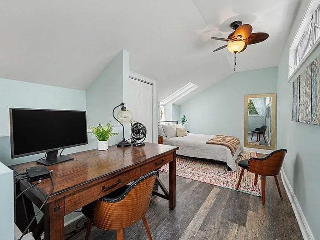 A compact bedroom with a bed, a desk, a chair, a television, and a ceiling fan.