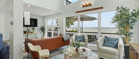 A spacious living room with a large window, a round glass coffee table, and a comfortable seating area.