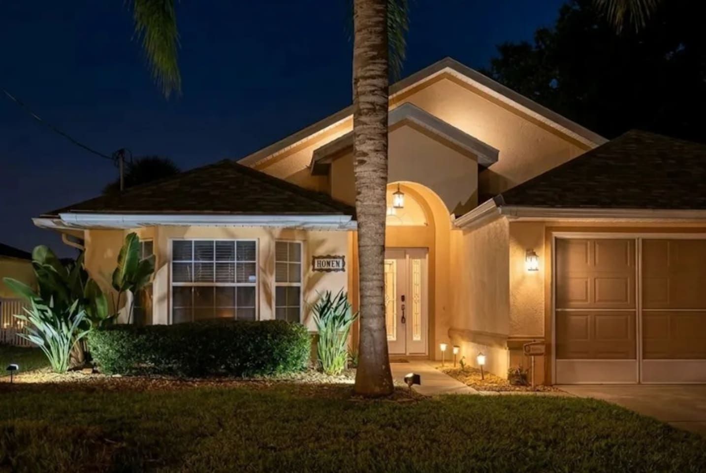 A residential house with a garage, a well-lit entrance, and a sign that reads 'HONEY'.