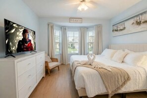 Ein Schlafzimmer mit einem Bett, einem Fernseher auf einer Kommode, einem Sessel und einem Schild mit der Aufschrift 'BEACH'.