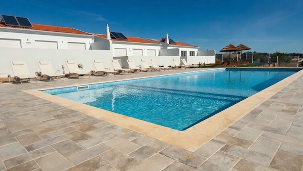 A swimming pool with lounge chairs and umbrellas, a white building with a red roof, and a clear blue sky. - Vrbo Property (Silves)