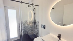 A modern bathroom with a glass shower enclosure, a round mirror, and a white sink. - Vrbo Property (Silves)