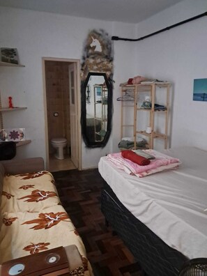 Ein Schlafzimmer mit einem Bett, einer Holzkommode, einem Spiegel, einem Kleiderschrank und einer Badezimmertür.