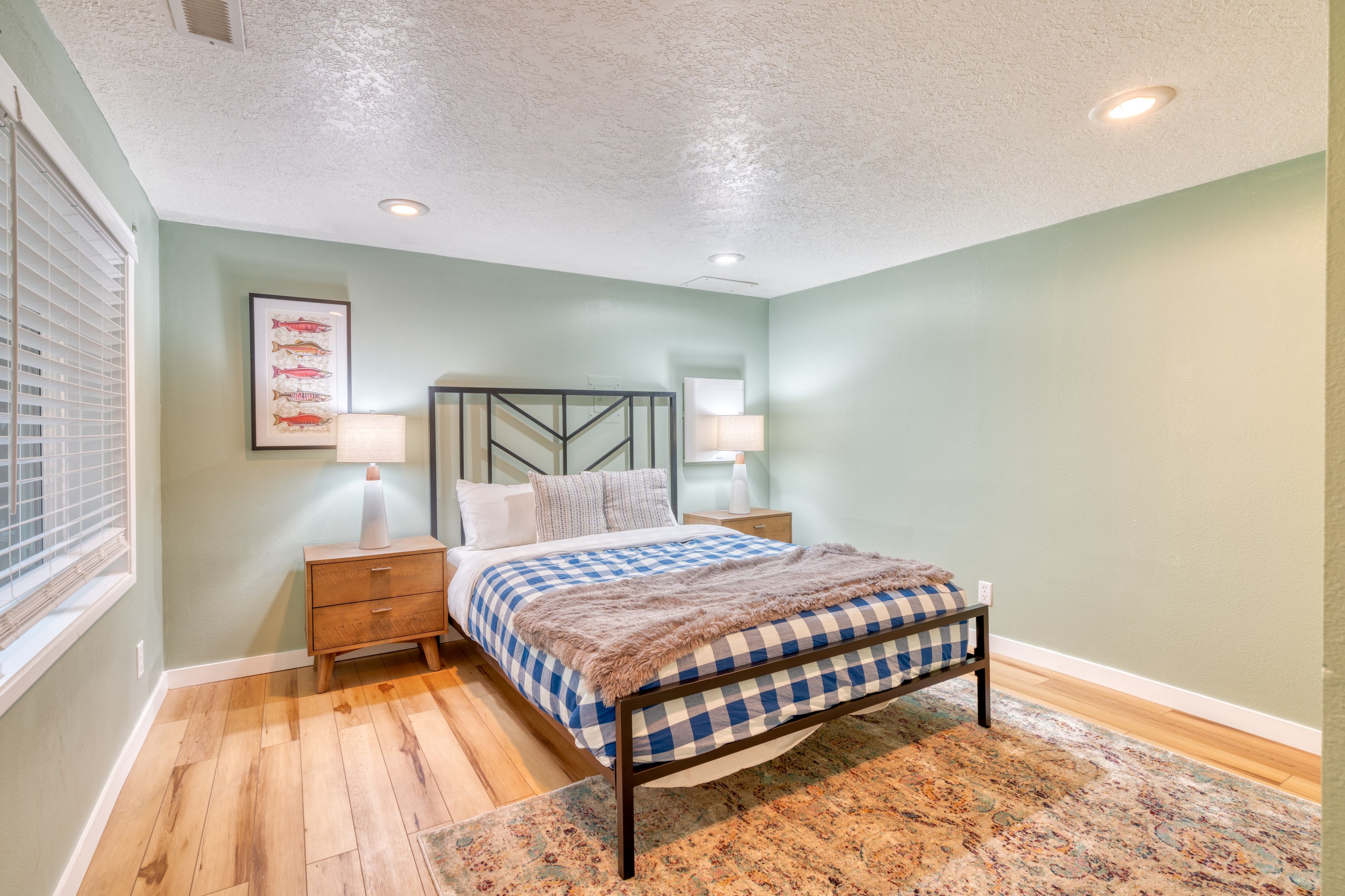 Une chambre à coucher avec un lit, des tables de chevet, une lampe fixée au mur, un tableau représentant un poisson, et un tapis à motifs.