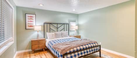 A bedroom with a bed, nightstands, a wall-mounted lamp, a framed fish picture, and a patterned rug.