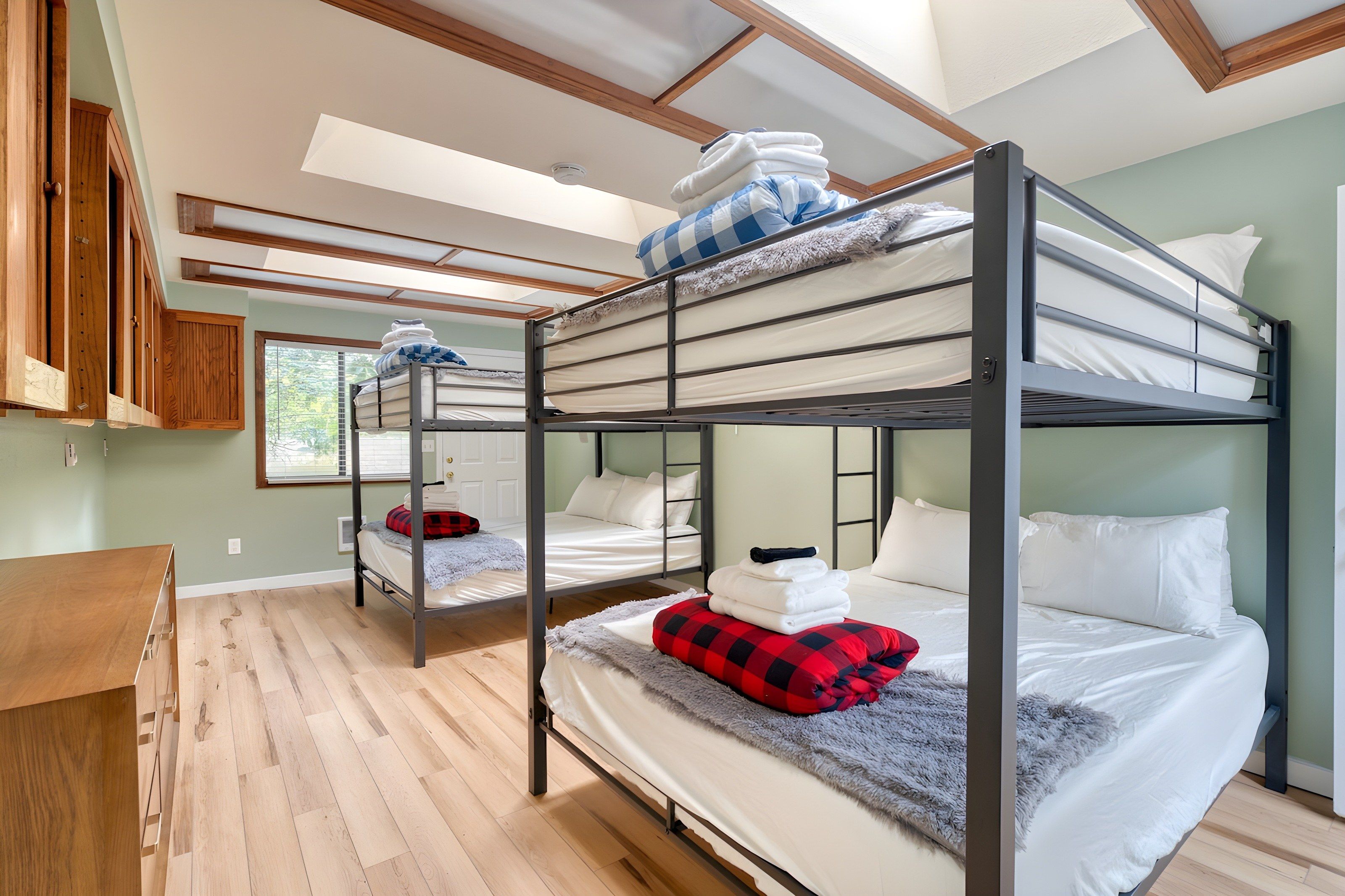 A bunk bed room with a wooden floor, a desk, and a window.