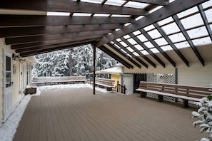 An outdoor wooden deck with benches, a covered area with a wooden roof, and a view of snow-covered trees.