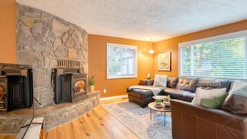 A living room with a stone fireplace, leather sofa, and large windows.