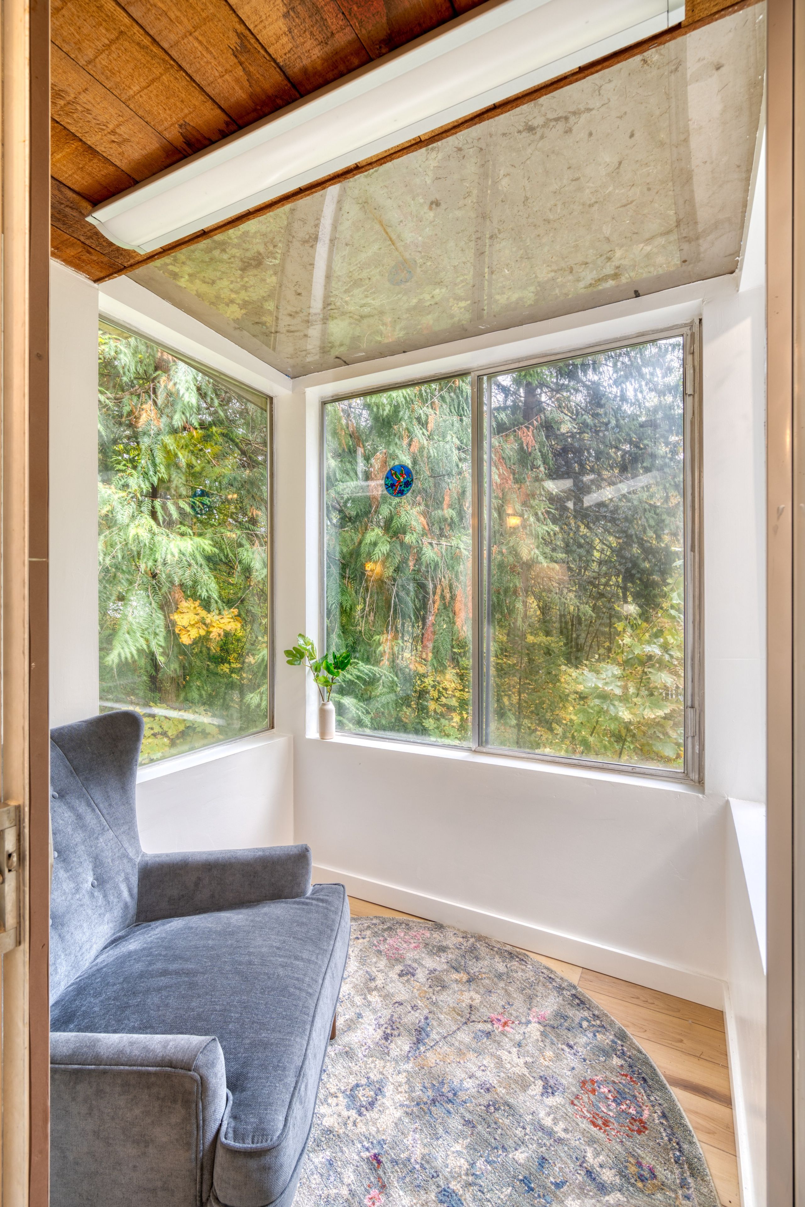 Ein Zimmer mit integriertem Fenster, einem grauen Sofa und einem gemusterten Teppich.