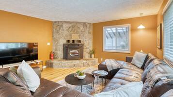 A living room with a stone fireplace, leather sofas, a flat-screen TV, and a large window with blinds.