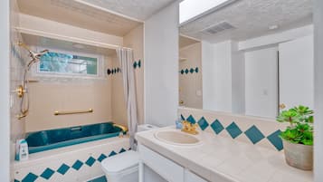 Et badeværelse med badekar, toilet, håndvask og en potteplante.