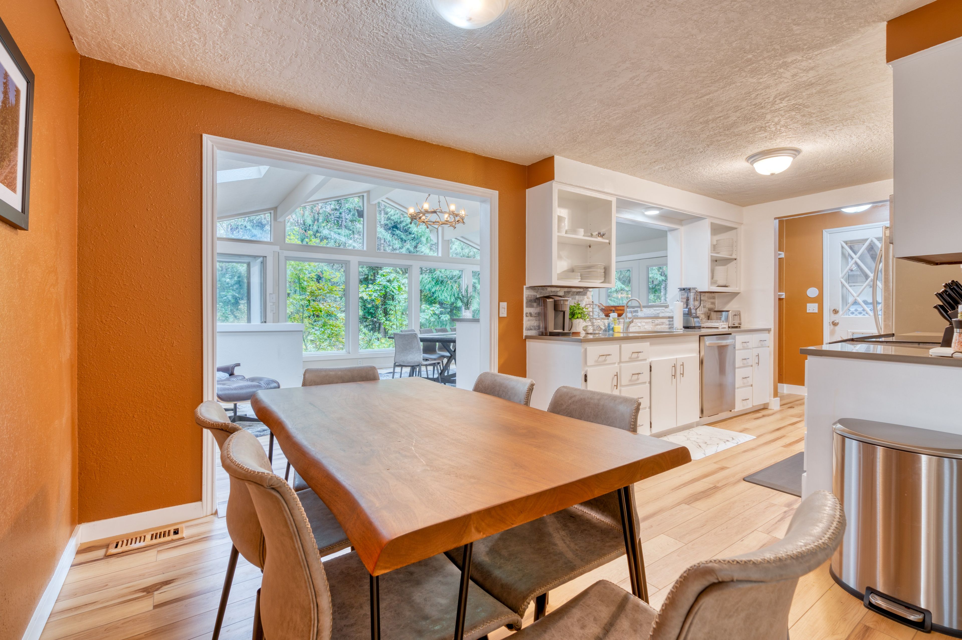 A modern kitchen with white cabinets, a stainless steel refrigerator, and a dining area with a wooden table and chairs.