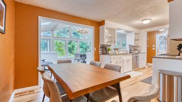 A modern kitchen with white cabinets, a stainless steel refrigerator, and a dining area with a wooden table and chairs.