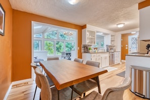 A modern kitchen with white cabinets, a stainless steel refrigerator, and a dining area with a wooden table and chairs.