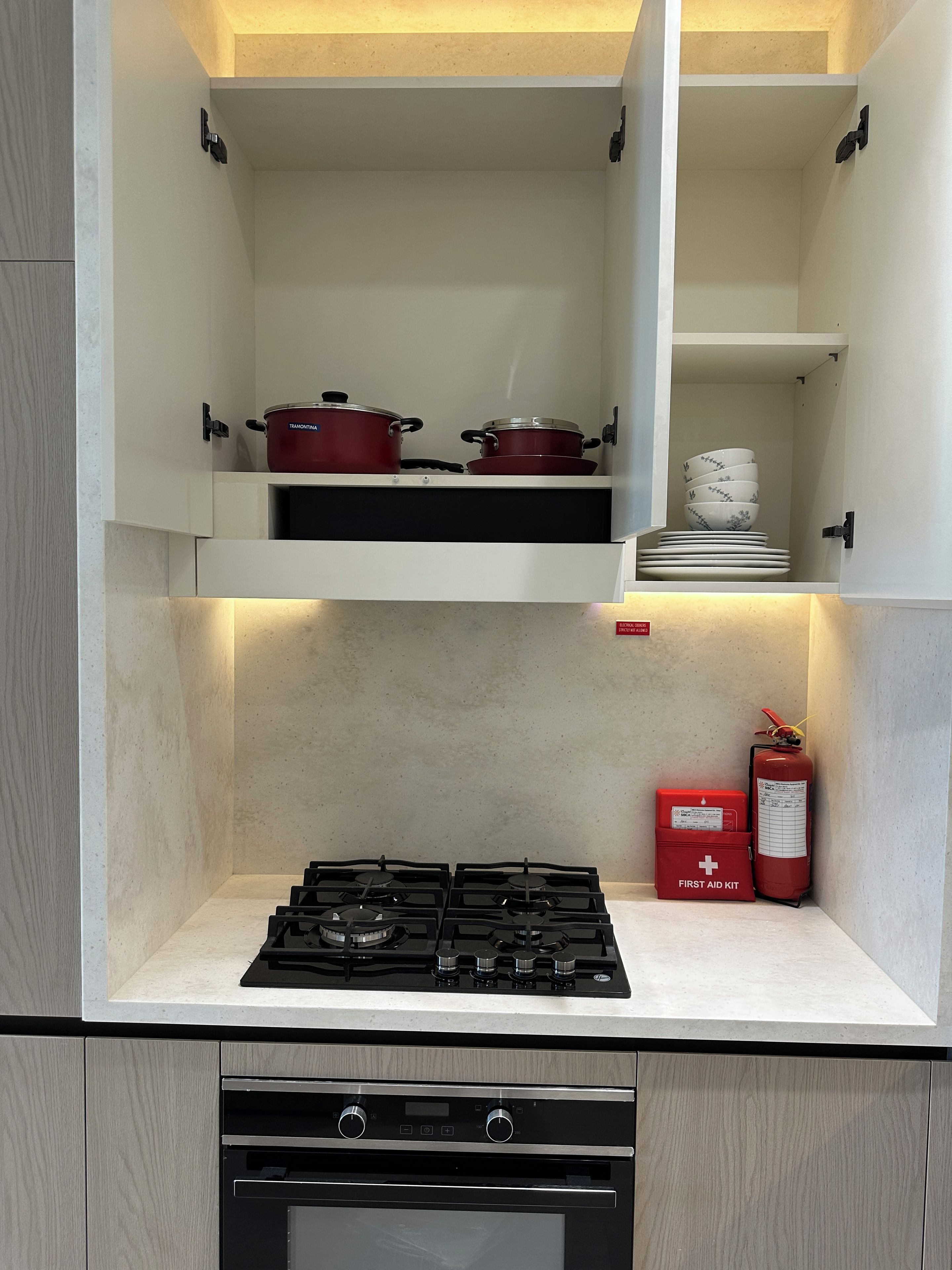 Une cuisine équipée d’une cuisinière à gaz, d’une trousse de premiers secours et de casseroles rangées sur l’étagère supérieure.
