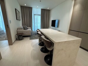 Un espacio habitable moderno con sofá, zona de comedor con taburetes de bar, televisor de pantalla plana y ventana grande con cortinas.