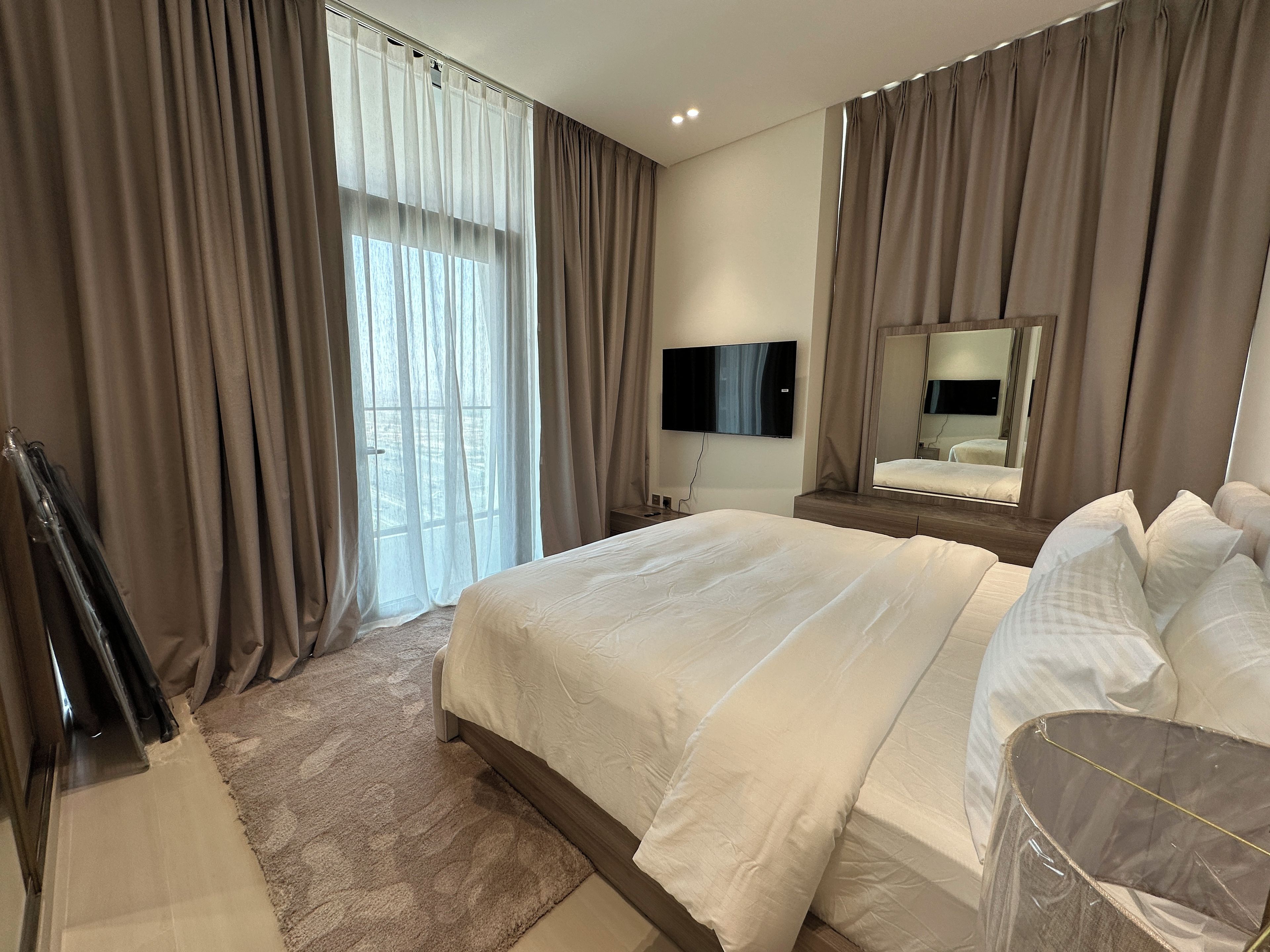 Une chambre d’hôtel avec un grand lit, un téléviseur à écran plat, un miroir et une fenêtre avec des rideaux.