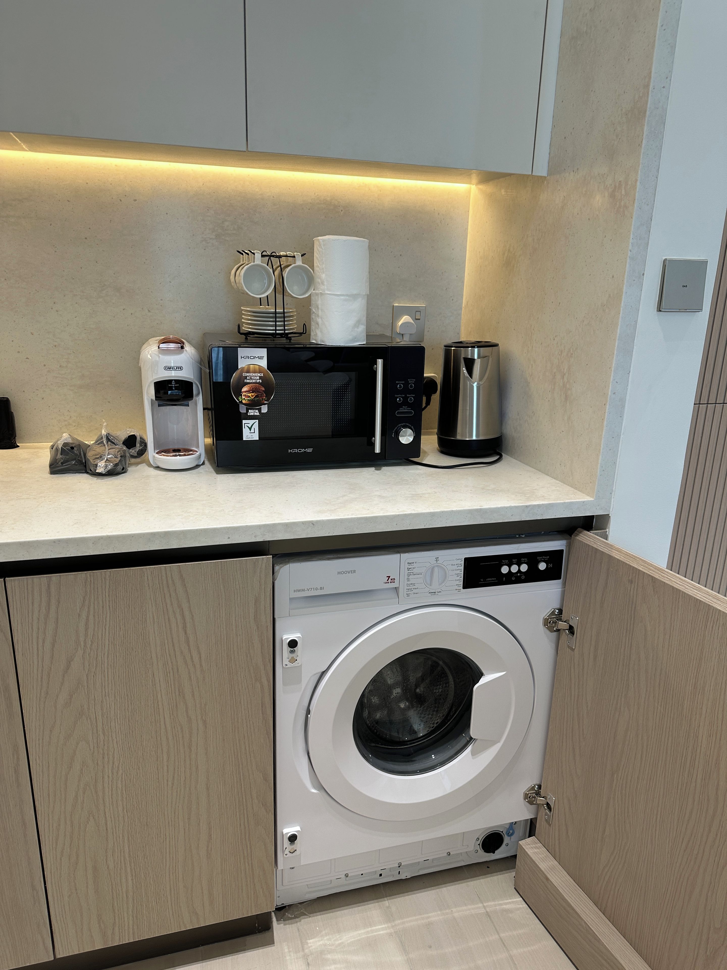 Une petite cuisine équipée d’un four à micro-ondes, d’une machine à café et d’un lave-linge encastré.