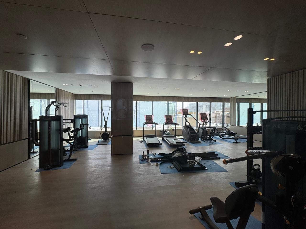 A gym with various exercise equipment, large windows, and a high ceiling.