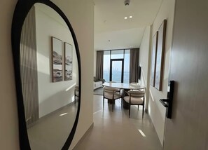 A hotel room with a large mirror, a dining area with a table and chairs, and a view of the city through the window.