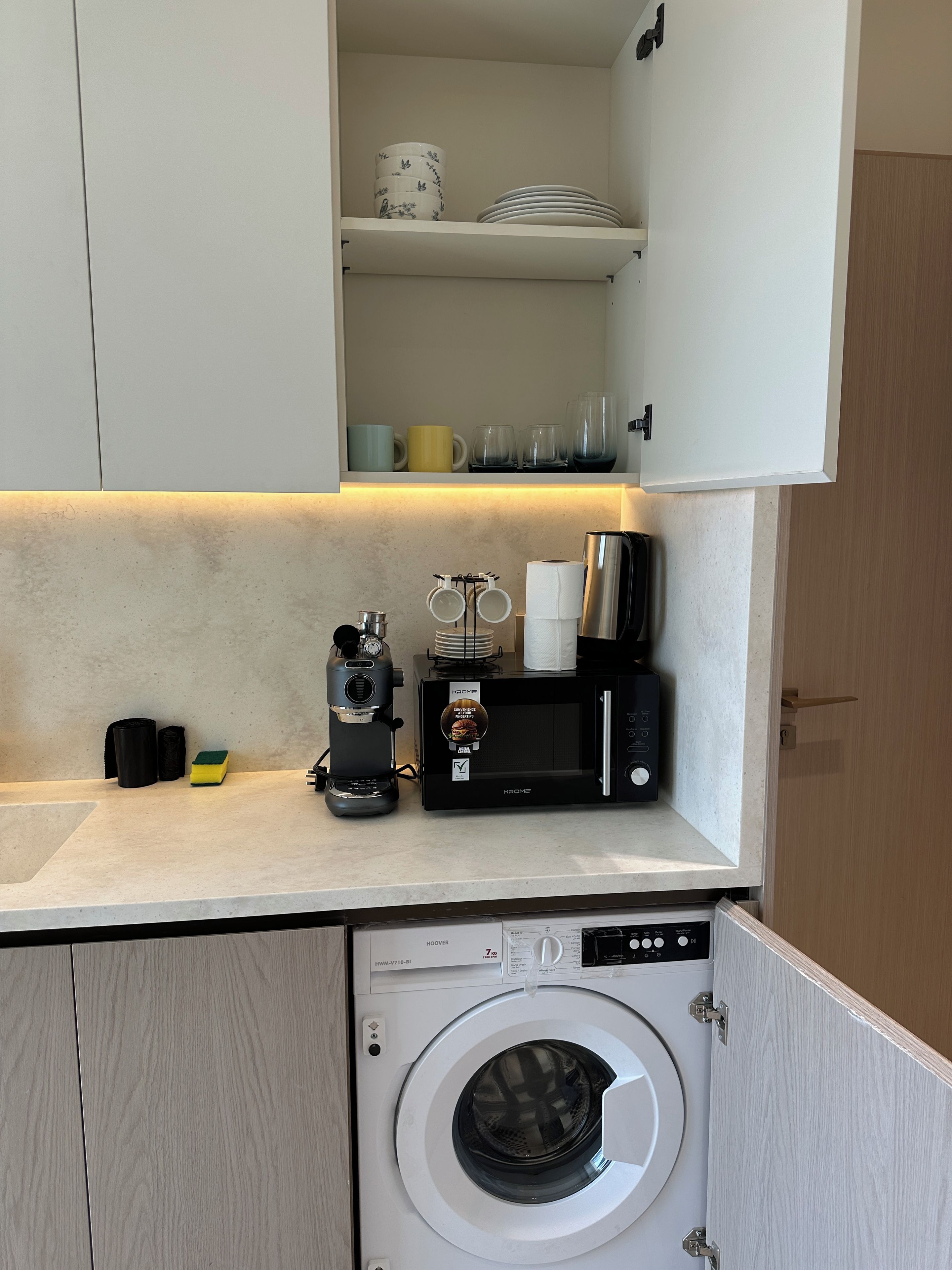 A compact kitchen with a coffee maker, microwave, and washing machine.