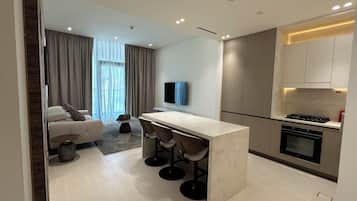 A modern kitchen with a central island, bar stools, a built-in oven, and a flat-screen TV mounted on the wall.