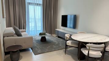 Un salon moderne comprenant un canapé, une table basse, une table à manger avec des chaises, un téléviseur à écran plat et une grande fenêtre avec des rideaux.
