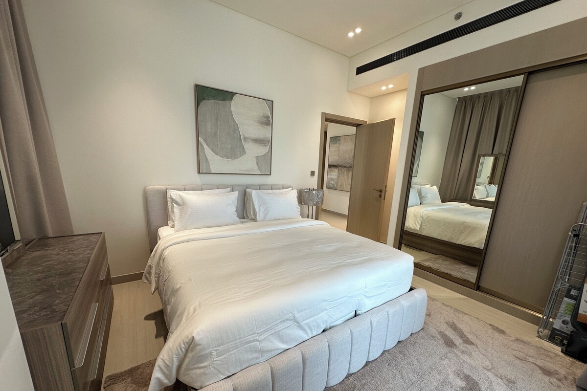 A modern bedroom with a large bed, a wardrobe, and a mirror.