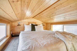 Ein Schlafzimmer einer Holzhütte mit einem Bett, Kissen und einem Fenster.