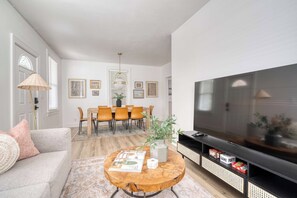 Una sala de estar con sofá, mesa de centro, mueble para televisión y comedor.
