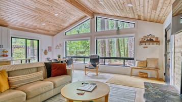 A spacious living room with a high ceiling, large windows, a sofa, a coffee table, and a chair.