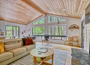 A spacious living room with a high ceiling, large windows, a sofa, a coffee table, and a chair. - Forest Cabin Retreat - Dog Friendly - Hot Tub (Rhododendron)