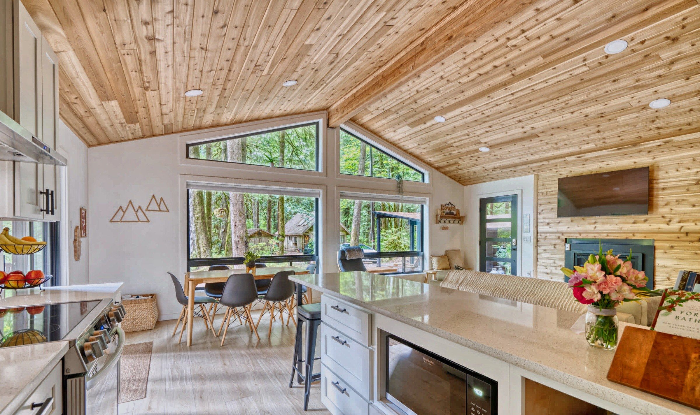 Eine moderne Küche mit Holzbalkendecke, großen Fenstern und einem Essbereich mit Blick ins Freie.