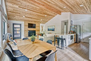 A modern kitchen with a wooden ceiling, a dining area with a wooden table and chairs, and a living space with a sofa and fireplace. - Forest Cabin Retreat - Dog Friendly - Hot Tub (Rhododendron)